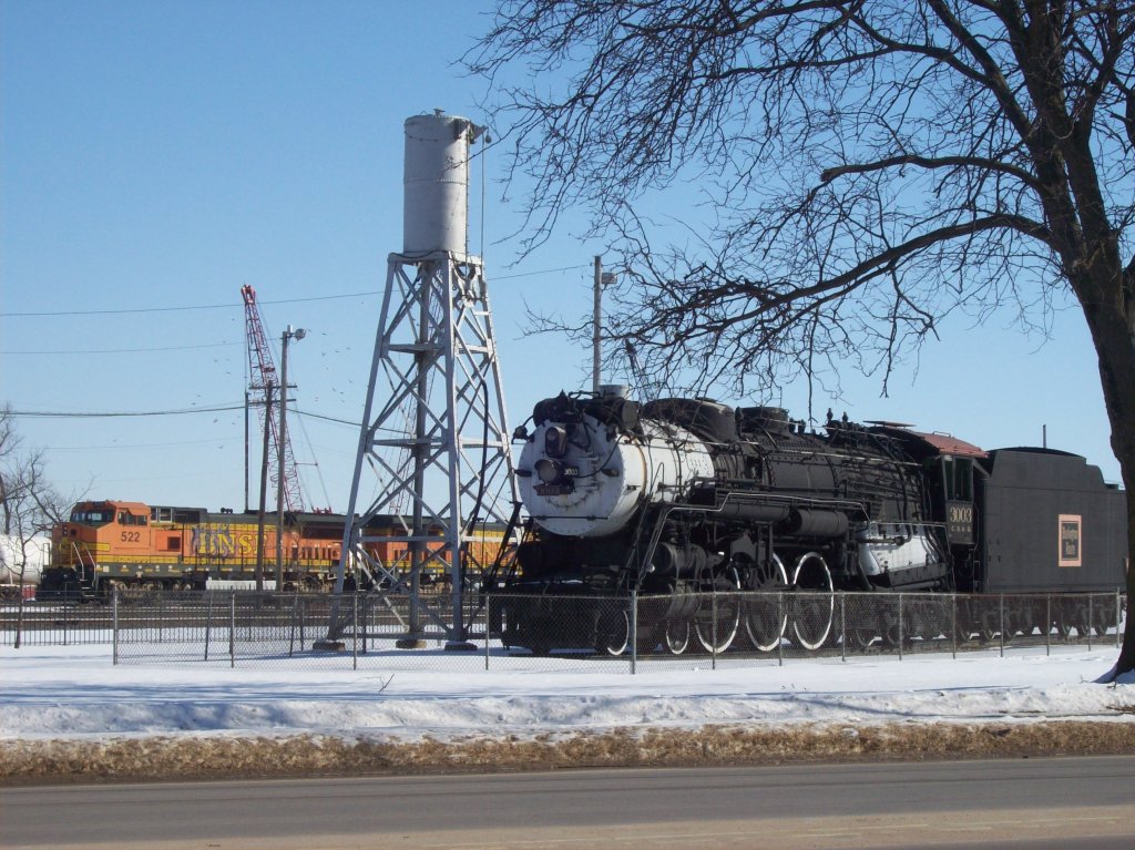 Chicago, Burlington & Quincy 4-6-4 Hudson no. 3003 and a sand tower partially block former Santa Fe BNSF 522 and an unknown number diesel locomotive. The 3003 rests at the Burlington, Iowa depot since 1961.