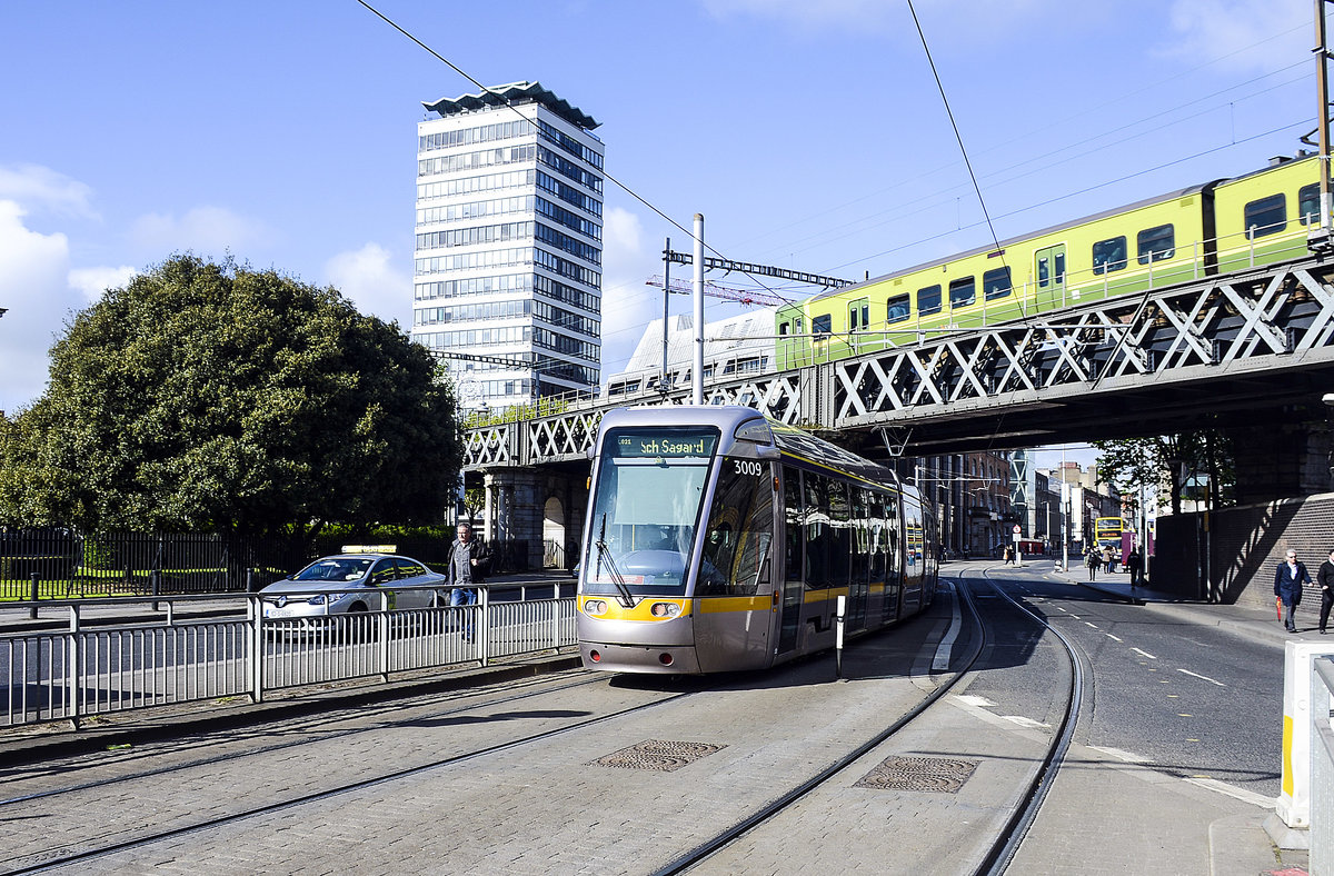 Tram LUAS 3009 at Beresford Place. On the elevated railway a electric multiple unit from Dublin Area Rapid Transit in the 8500 class passes the tram. Date: 10. Mai 2018.