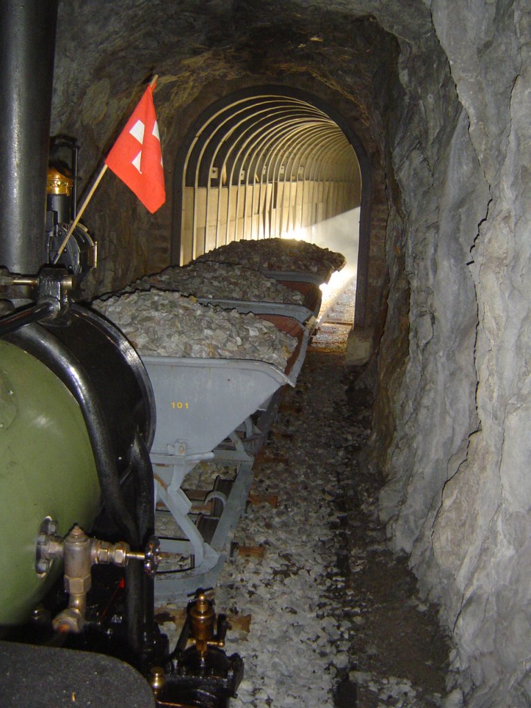 2 ft gauge steam engine  Liseli  (Jung No 1693, built 1911) in service on the high alpin panoramic railway of  Parc d'Attractions du Chatelard (VS)  in Switzerland. Traversing tunnel No 4 with a ballast train. To see in the background is a gallery; the sun light gives an imput to the scenery. The picture was taken from the locomotive platform running backwards to the station  Pied du barrage ; it is clear, walking to foot trough the tunnels is very dangerous and because of that strong forbidden. 21 Oct 2007