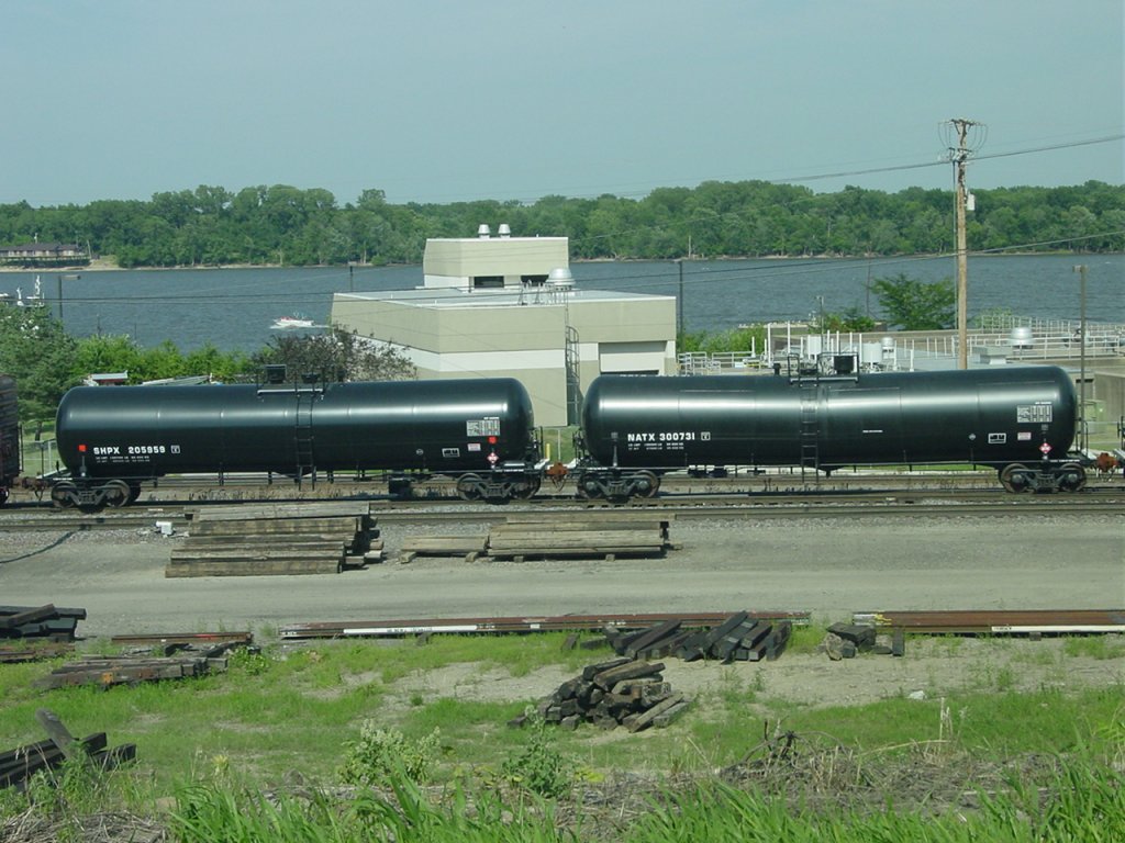 A pair of brand new tank cars roll thru the yard at Burlington, Iowa on 26 July 2003. One is marked SHPX, the other NATX. Mississippi River is in the background.