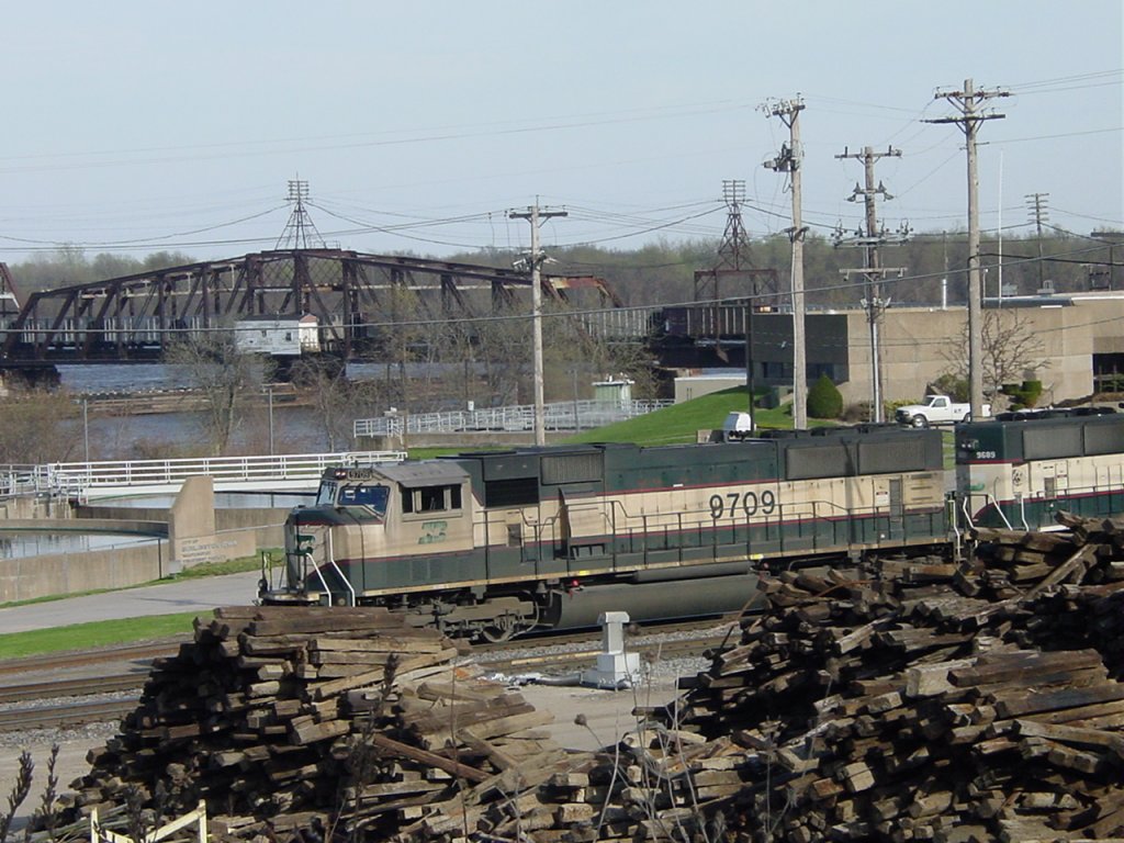 Burlington Northern 9709 & 9689 pull an empty coal train across the Mississippi River and into the yard at Burlington, Iowa on 9 Apr 2005. The bridge swing span and tender shack are visible just above the lok cab. The other building is the sewage treatment plant.