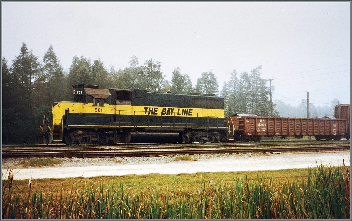 Bay Line Railroad EMD GP38 501 (second generation) shunted freight cars in Panama City, Florida. The Type B-B Road Switcher diesel locomotive was built in August 1969 by Electro Motive Division (EMD) under the serial number EMD 35170. I interpret “Road Switcher” as a mainline and shunting locomotive. A smaller CV of the locomotive: built for the Gulf, Mobile & Ohio with number 707, later to Illinois Central Gulf with number 9526, subsequently to Paducah & Louisville with number 2000 and from 1990 to the Bay Line with number 501 ; The number 501 was previously occupied by the GP7 from 1952.

The Bay Line Railroad was founded in the early 20th century. At that time, traffic in the ports increased steadily and a modern port was built in Panama City, Florida. This subsequently required a railway line to transport the goods to and from it, which was then built from Panama City to Atlanta, but was never able to have the successful traffic that was expected. The Bay Line Railroad today runs between Panama City (Florida) and Dothan (Alabama) with a branch from Grimes to Abbeville (Alabama). The main line was built in 1908 by the Atlanta & Saint Andrews Bay Railroad (ASAB), with the idea of ​​connecting Atlanta to the to connect the port of Panama City, but this goal was never achieved. Nevertheless, the railway was able to maintain a relatively short freight service. At times there was even passenger traffic. The Stone Container Corporation purchased the line from the Atlanta & Saint Andrews Bay in 1987 and sold it in 1994 to the Rail Management Corporation, which formed the new Bay Line Railroad company. Genesee & Wyoming acquired the assets including the Bay Line Railroad in 2005. The following goods are transported on the route, which is now 154 miles long: chemicals, coal, food and feed, forest products, ores and minerals, steel and scrap. Analogue picture from November 1992