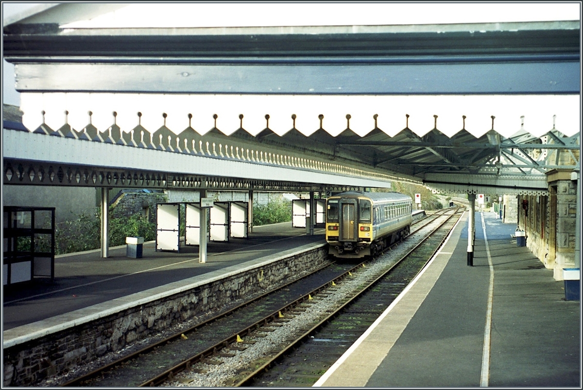 Tenby / Dinbich-y-pysgod a little station in Wales wiht a class 153 on the way to  Swansae / Abertawe.

Analo picture / Nov. 2000