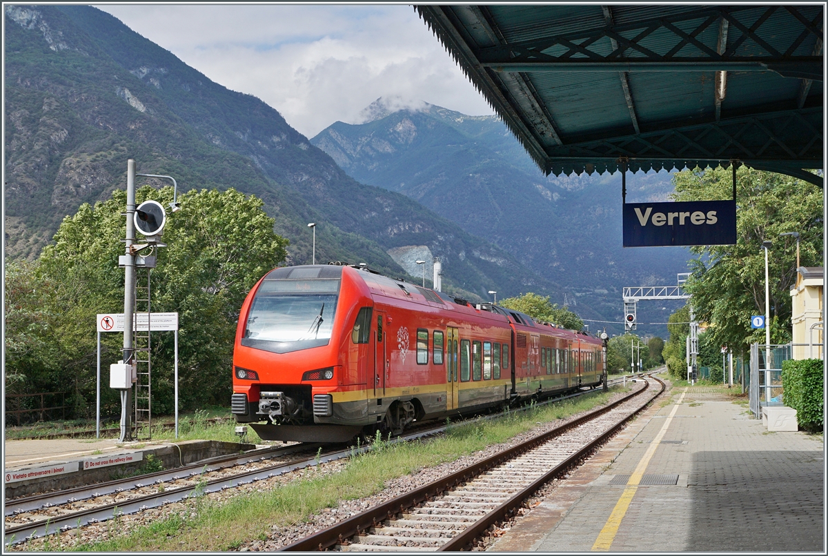 The bi-modular FS Trenitalia BUM BTR 831 001 leaves the stop at Verres station. This train is on its way from Torino Porta Nuova to Aosta. The train can be operated with diesel engines or electrically with 3000 volts direct current and has the wheel arrangement Bo' 2'2'2' Bo'. From Turin to Ivrea he uses the overhead line, from Ivrea he uses diesel. 

September 17, 2023