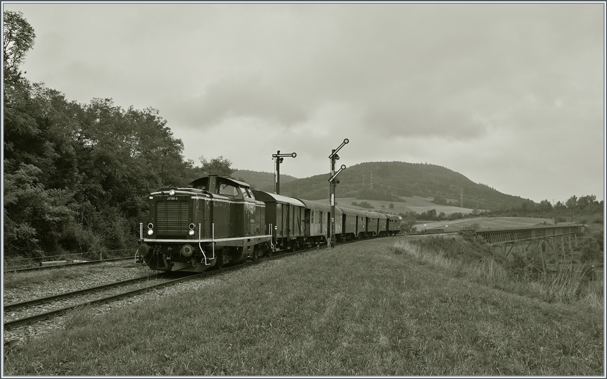 The diesel locomotive 211 041-9 (92 80 1211 041-9 D-NeSA) leaves Epfenhofen with its  morning train , in the background the  Talübergang Epfenhofen Bridge  which is the longest bridge on the Sauschwänzlebahn with a length of 264 meters. August 27, 2022