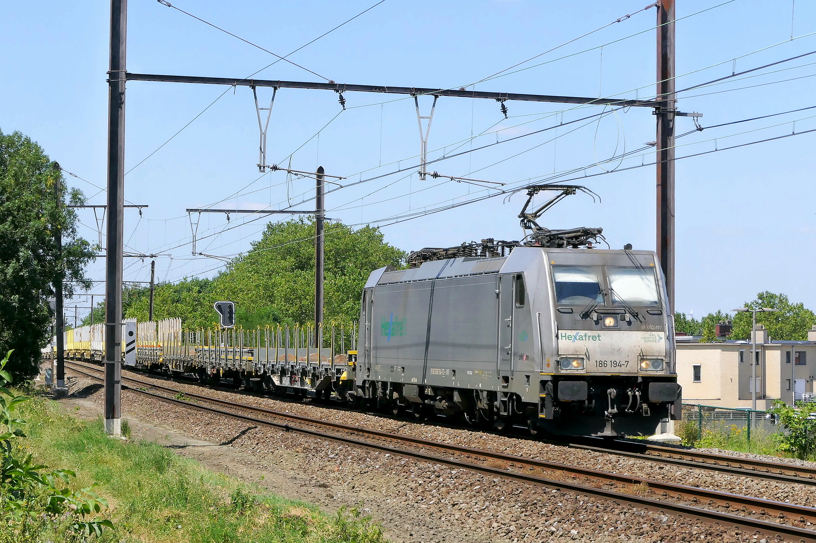 The Hexafret 186 194-7 with an empty flat stake goods wagons train from the port of Antwerp back to France. Bombardier Traxx F140 MS build in 2016 with construction N� 35364. Line 27A at Antwerp Airport. 15-07-2026