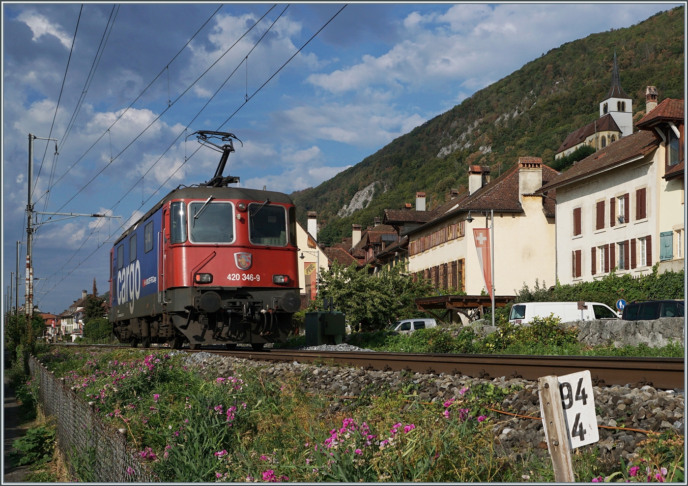 La Re 4/4 II 11346 (Re 420 346-9) des CFF est en route en tant que train tracté par locomotive près de Ligerz en direction de Neuchâtel. Sur le côté gauche de l'image, les charmantes maisons de Ligerz sont visibles, et même l'église peut être aperçue (légèrement masquée).

24 août 2026