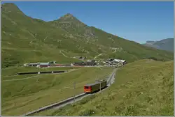 A small train in a magnificent mountain landscape: A Jungfrau Railway (JB) BDeh 4/4 with Bt has left Kleine Scheidegg, visible in the background, and is now on its way to the highest railway station